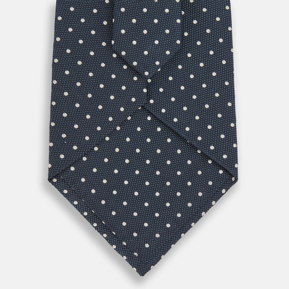 The Turnbull & Asser Navy Micro Dot Silk Tie features a handmade navy blue silk fabric with evenly spaced small white dots, rolled up on a plain white background—a timeless formal accessory for any event.