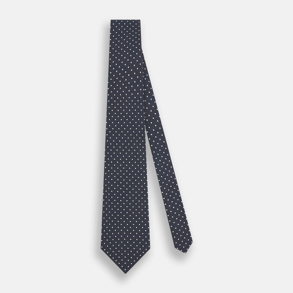 The Turnbull & Asser Navy Micro Dot Silk Tie features a handmade navy blue silk fabric with evenly spaced small white dots, rolled up on a plain white background—a timeless formal accessory for any event.