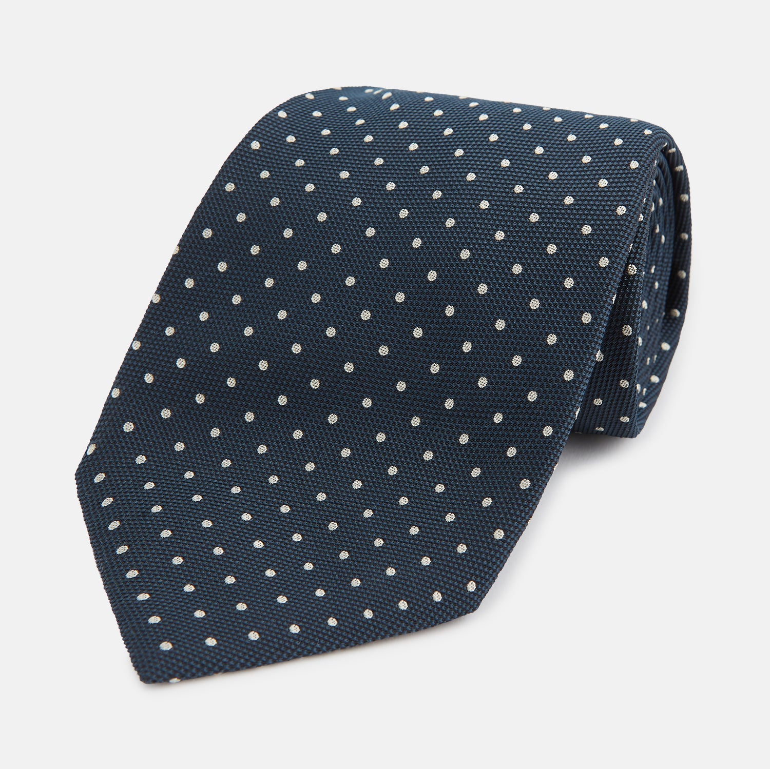 View 1 of product The Turnbull & Asser Navy Micro Dot Silk Tie features a handmade navy blue silk fabric with evenly spaced small white dots, rolled up on a plain white background—a timeless formal accessory for any event.