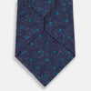View 3 of product The Turnbull & Asser Navy Floret Silk Tie features a rolled-up deep blue silk fabric with a textured finish and small teal dot details, shown against a white background.