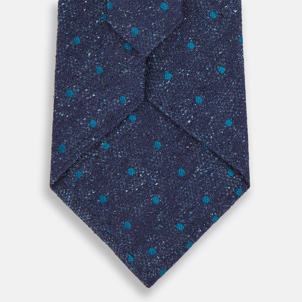 The Turnbull & Asser Navy Floret Silk Tie features a rolled-up deep blue silk fabric with a textured finish and small teal dot details, shown against a white background.