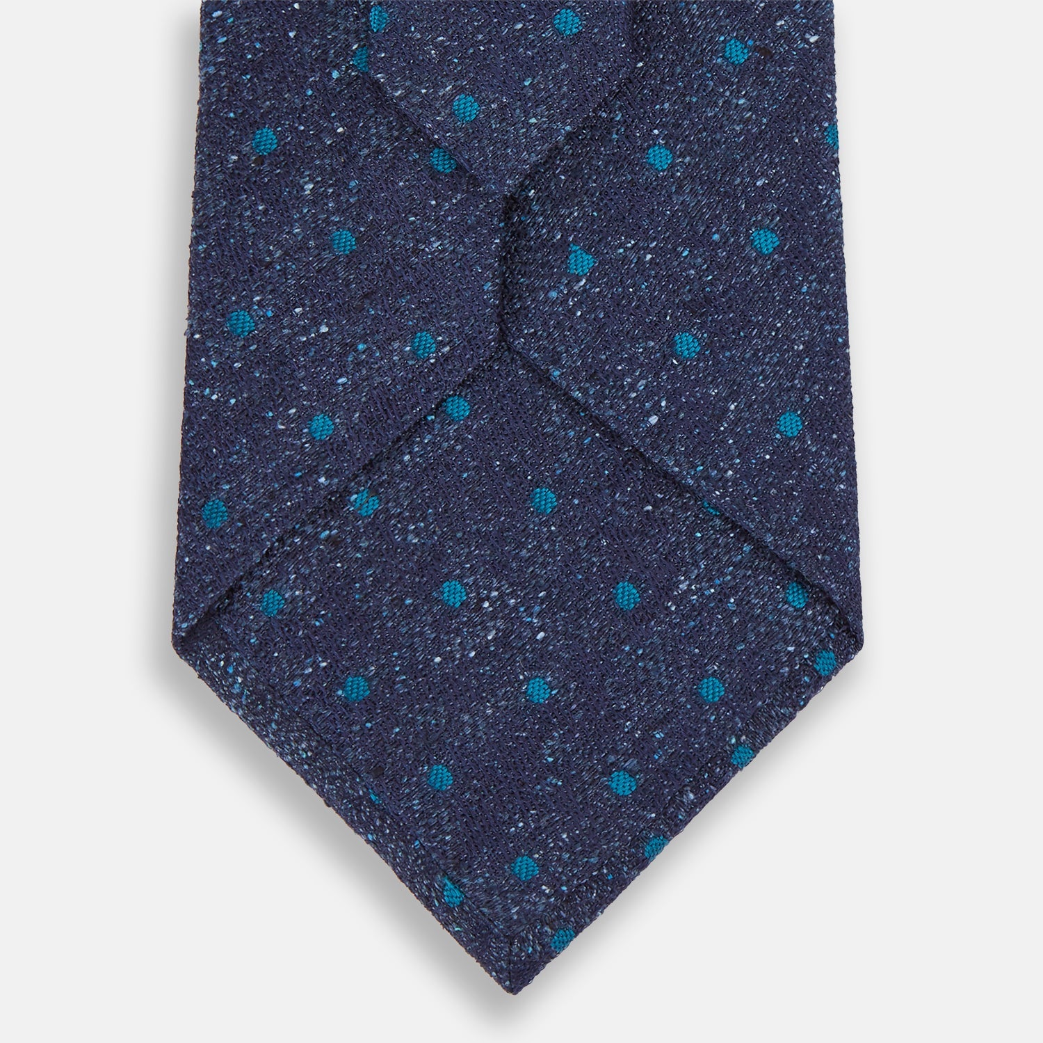 View 3 of product The Turnbull & Asser Navy Floret Silk Tie features a rolled-up deep blue silk fabric with a textured finish and small teal dot details, shown against a white background.