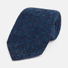 View 1 of product The Turnbull & Asser Navy Floret Silk Tie features a rolled-up deep blue silk fabric with a textured finish and small teal dot details, shown against a white background.