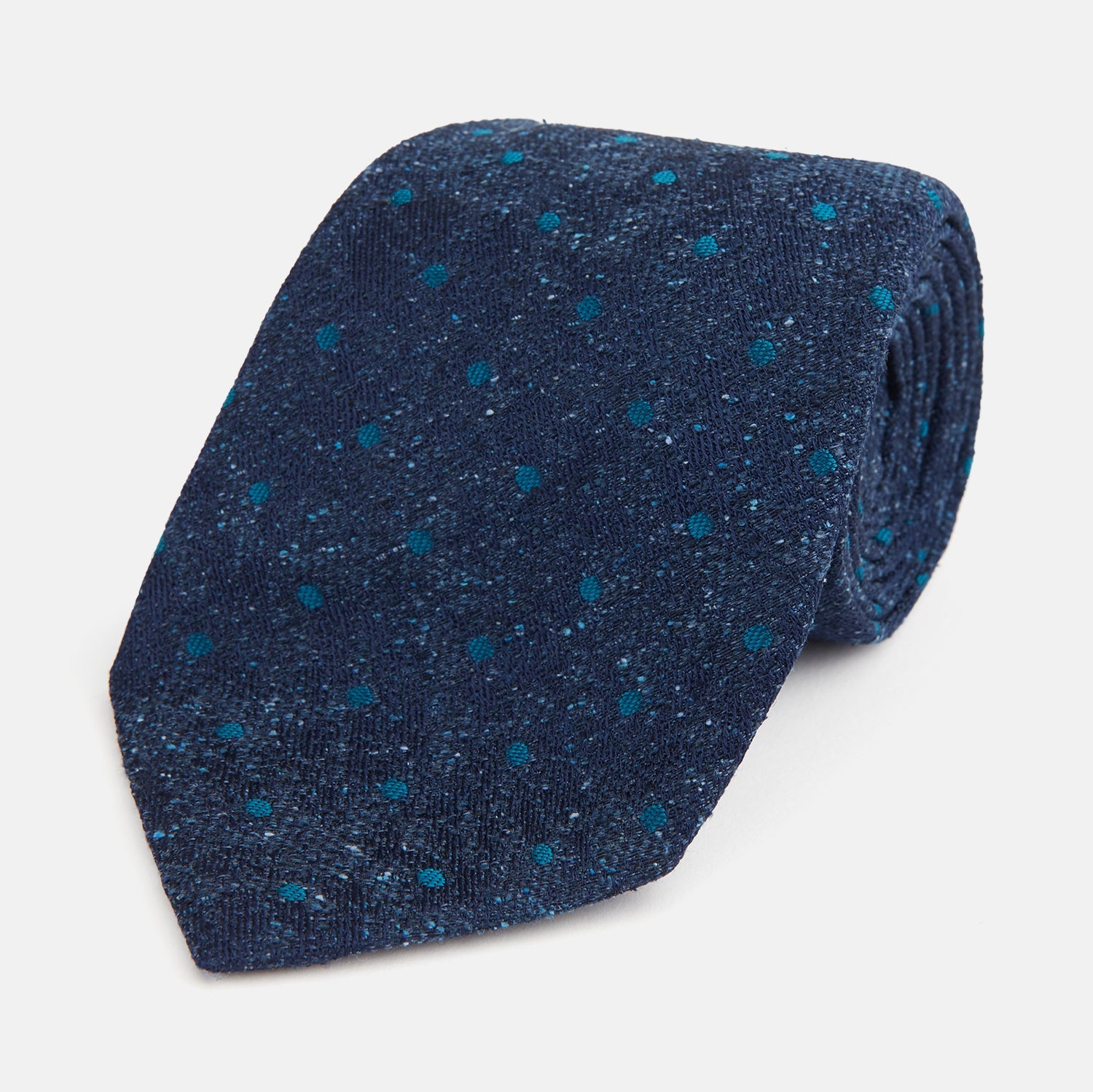 View 1 of product The Turnbull & Asser Navy Floret Silk Tie features a rolled-up deep blue silk fabric with a textured finish and small teal dot details, shown against a white background.