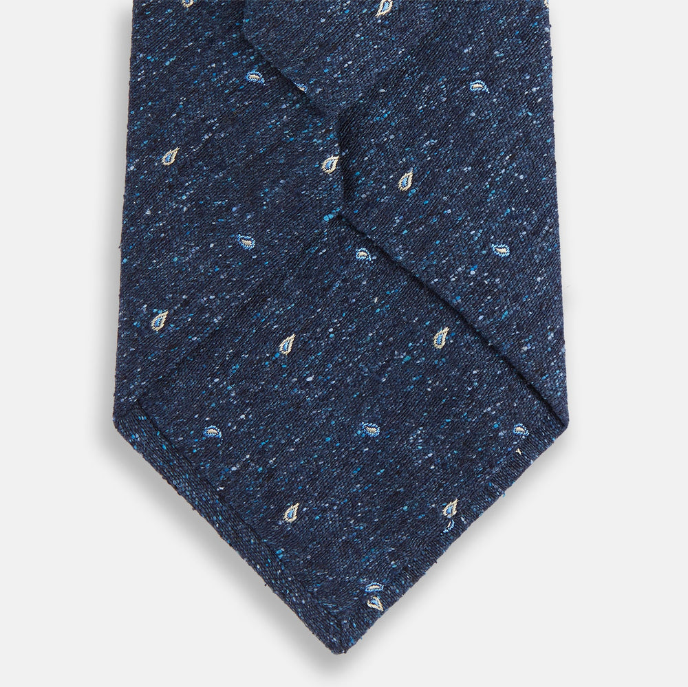 The Turnbull & Asser Navy Micro Paisley Silk Tie features a rolled-up navy blue silk with a subtle speckled texture and small light blue paisley patterns, perfect for enhancing any formal collection, shown on a white background.