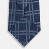 View 3 of product The Turnbull & Asser Navy Bold Double Check Silk Tie features a textured navy fabric with a light blue windowpane plaid pattern. This handmade silk tie is neatly rolled on a white background.