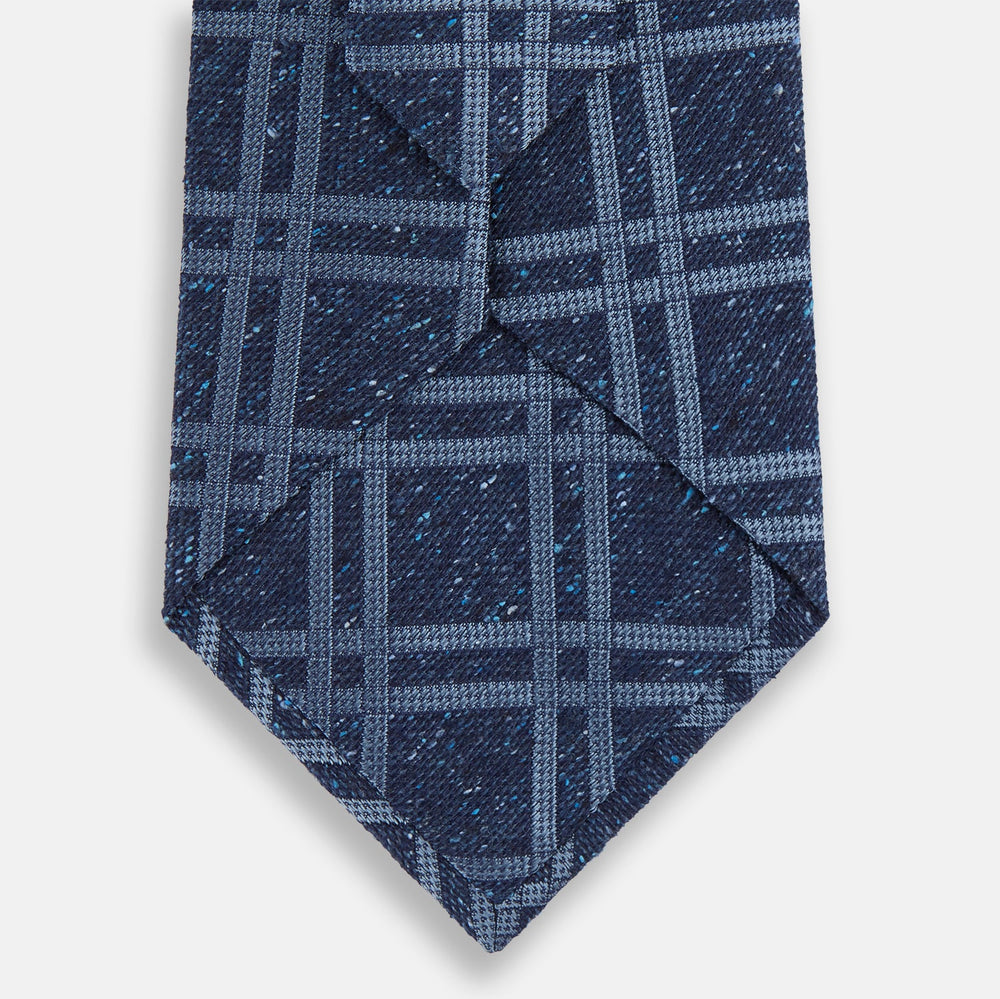 The Turnbull & Asser Navy Bold Double Check Silk Tie features a textured navy fabric with a light blue windowpane plaid pattern. This handmade silk tie is neatly rolled on a white background.