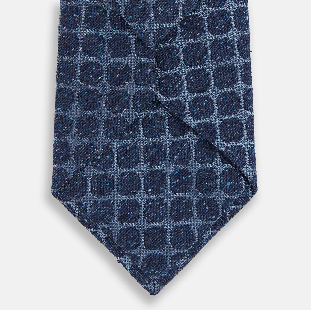 The Turnbull & Asser Navy Grid Silk Tie is handmade and neatly rolled, showcasing a dark blue silk fabric with a textured grid pattern, displayed on a plain white background.