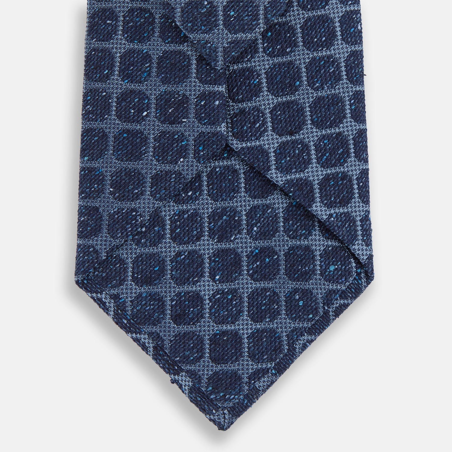 View 3 of product The Turnbull & Asser Navy Grid Silk Tie is handmade and neatly rolled, showcasing a dark blue silk fabric with a textured grid pattern, displayed on a plain white background.