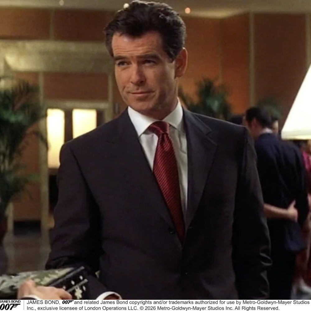 The Turnbull & Asser Die Another Day Stripe Silk Tie, as seen on James Bond, showcases a vibrant orange, red, and purple woven pattern, elegantly rolled and displayed against a white background.