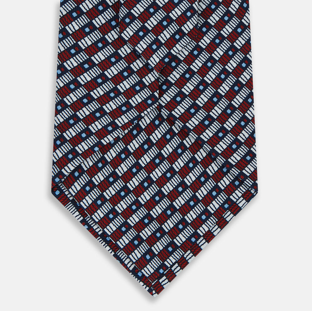 The Turnbull & Asser UK TIES 9.5CM GEOMETRIC RECTANGLES RED is an English silk tie with small red, navy blue, and white rectangles and dots on a white background.