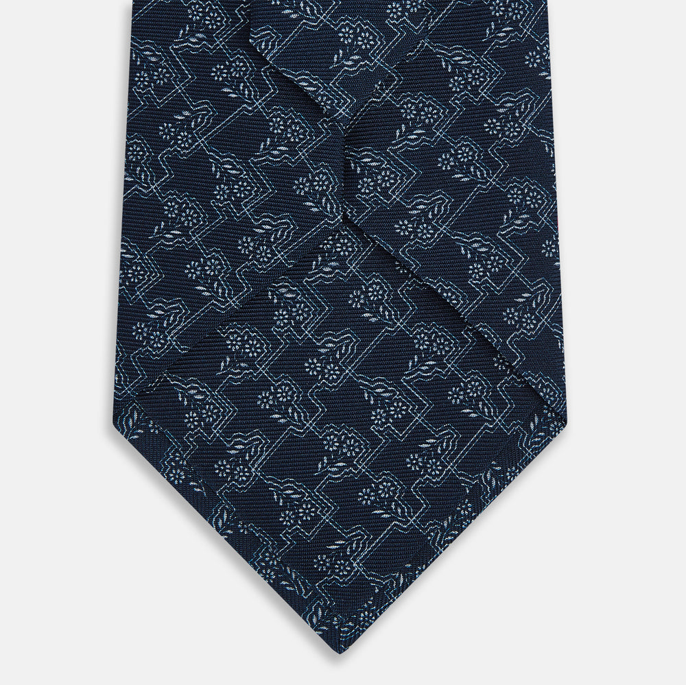 The Turnbull & Asser UK Midnight Blue Floral Jigsaw Printed Silk Tie features a light blue geometric and floral pattern on premium English silk, with a pointed tip and textured finish for an elegant touch.
