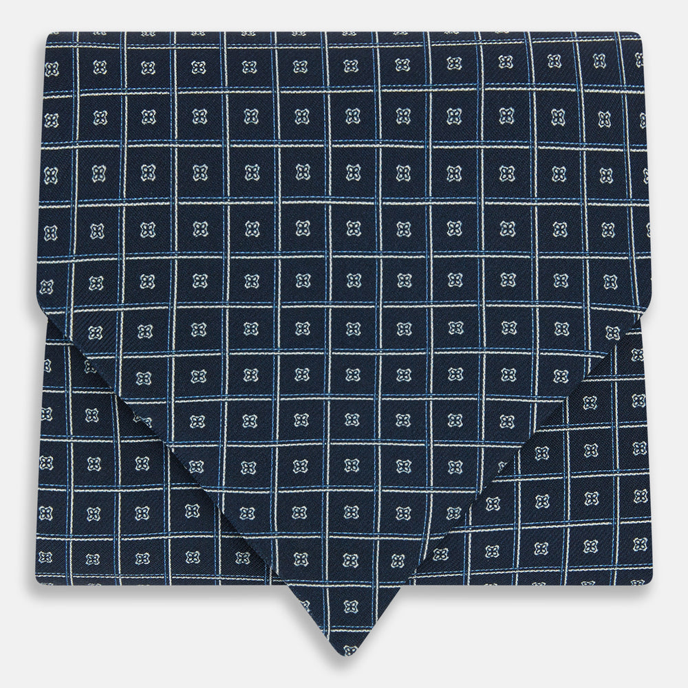A folded Geometric Navy Quatrefoil Motif Ascot Tie in Silk, featuring a navy ground with a white grid pattern and small quatrefoil motifs in each square.