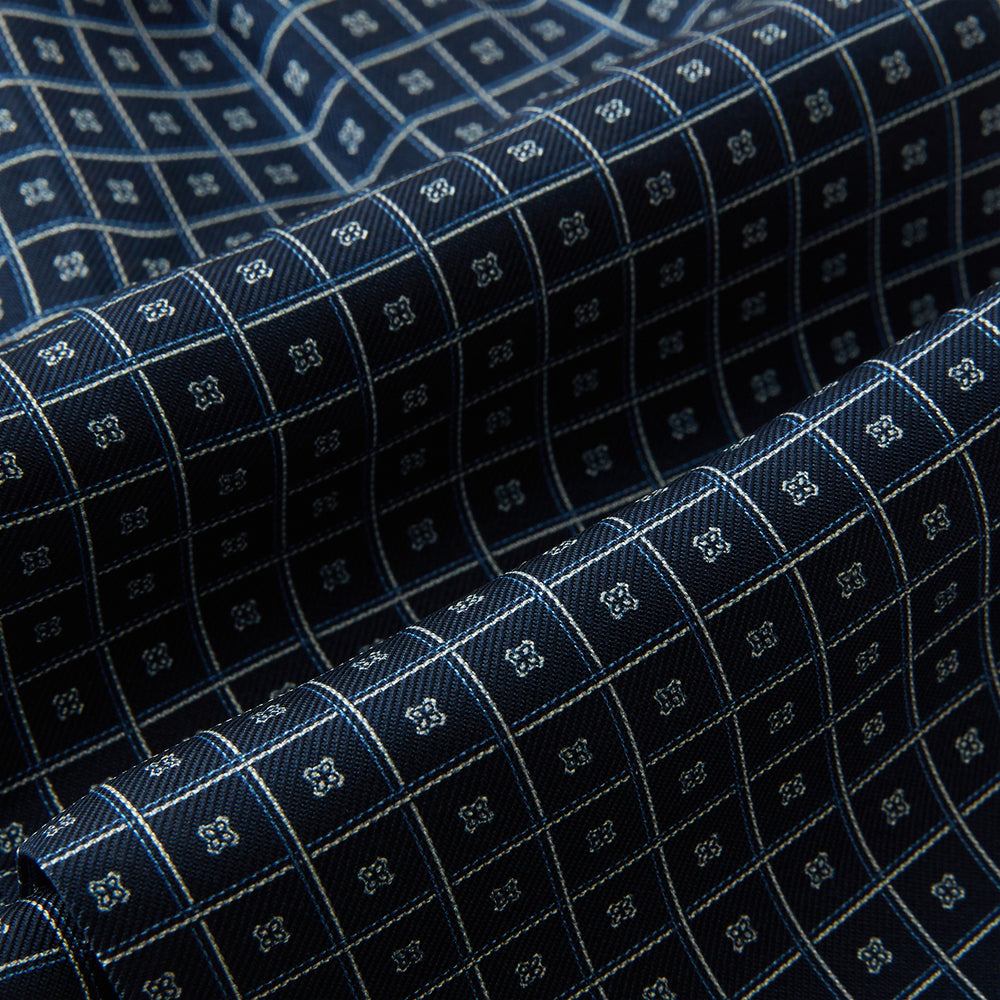 A folded Geometric Navy Quatrefoil Motif Ascot Tie in Silk, featuring a navy ground with a white grid pattern and small quatrefoil motifs in each square.