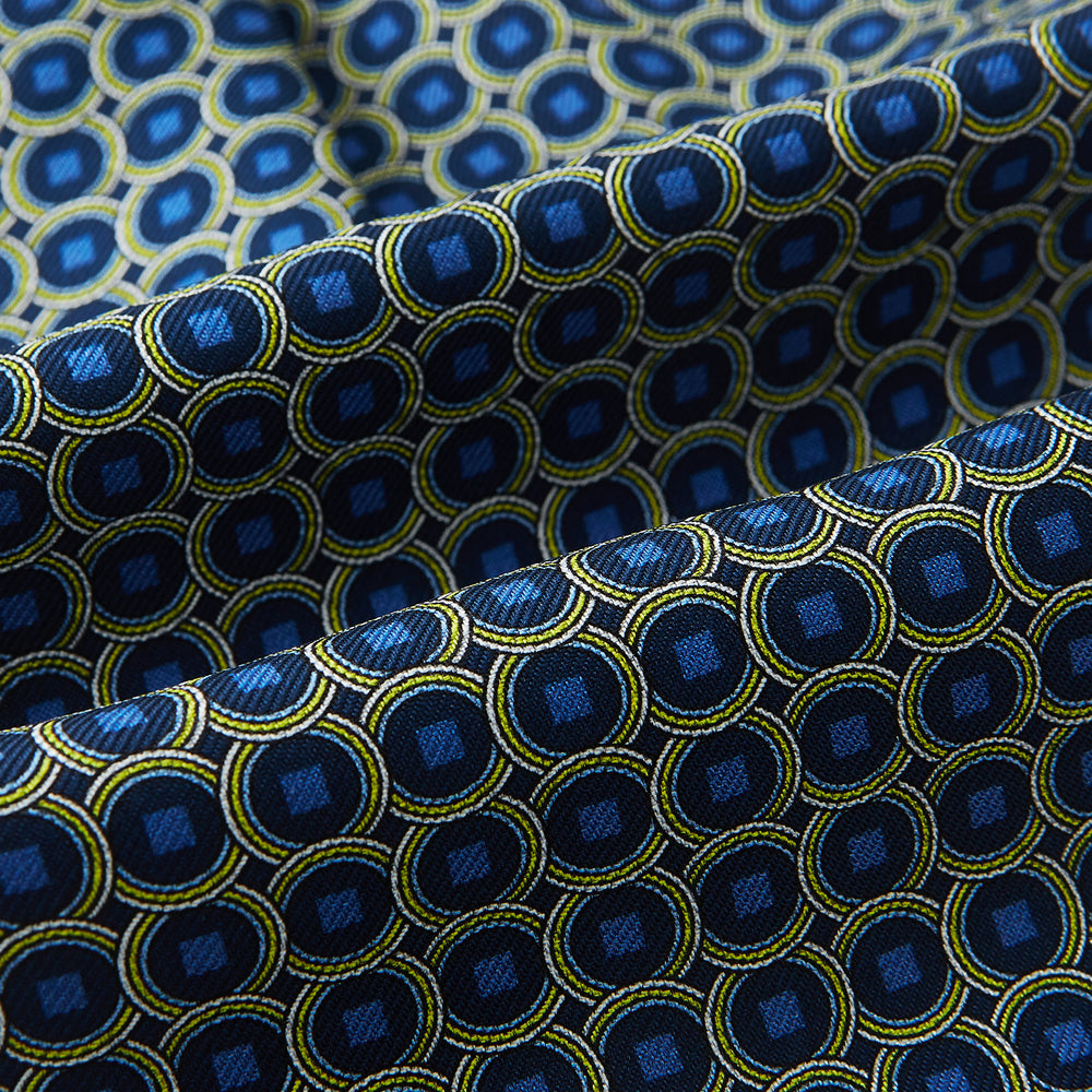 Close-up of Turnbull & Asser UK's Navy Interlocking Circle Foulard Silk Cravat, featuring a geometric pattern of yellow and blue circles and squares. Subtle folds add texture—ideal as a refined accessory inspired by classic British style.