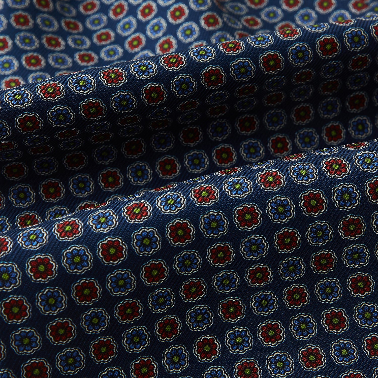 View 4 of product The Turnbull & Asser UK Midnight Blue Contrasting Rosette Medallion Printed Silk Cravat features a grid of small red, yellow, and blue floral patterns on textured silk—evoking classic British style.