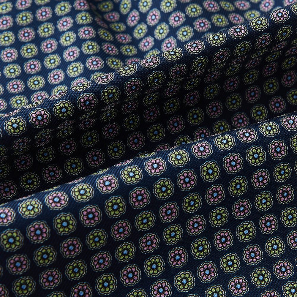 Close-up of the Turnbull & Asser UK Dark Navy Contrasting Rosette Medallion Printed Silk Cravat, featuring folded dark blue silk with a vibrant pattern of pink, yellow, and green rosette medallions.