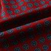 View 4 of product Close-up of the Turnbull & Asser UK Red Rosette Medallion Printed Silk Cravat, featuring blue and teal medallions on rich red silk. The fabric’s visible texture and folds showcase its intricate motif and classic British elegance.