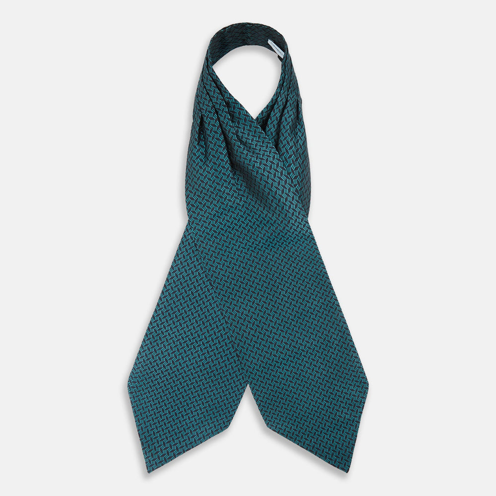 The Turquoise Geometric Silk Cravat by Turnbull & Asser features a striking teal and black pattern—perfect for those who appreciate bold, handmade neckwear with geometric flair.