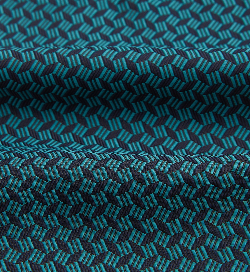 The Turquoise Geometric Silk Cravat by Turnbull & Asser features a striking teal and black pattern—perfect for those who appreciate bold, handmade neckwear with geometric flair.