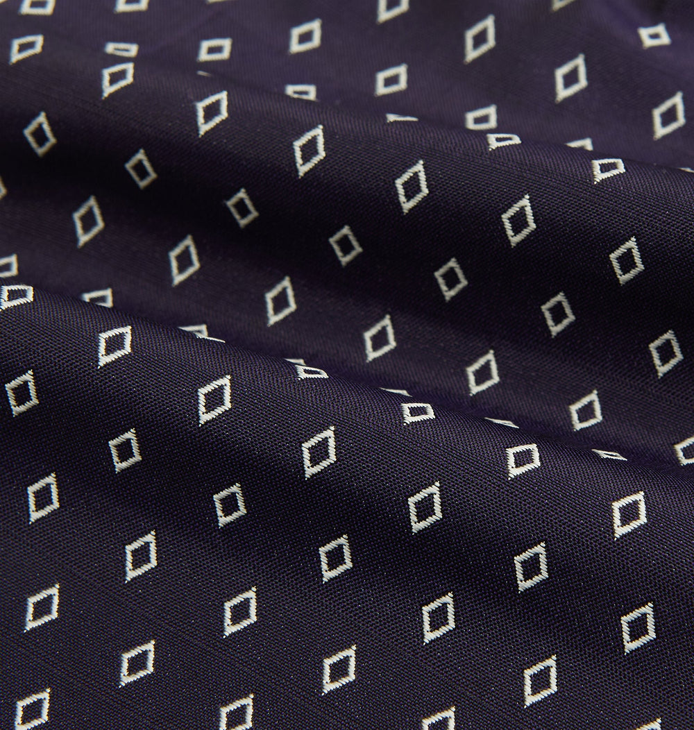 The Turnbull & Asser Blue Diamond Silk Cravat is a refined men's formal accessory, featuring a navy blue base with small white diamond patterns—perfectly complemented by a neatly folded, pointed-corner pocket square.