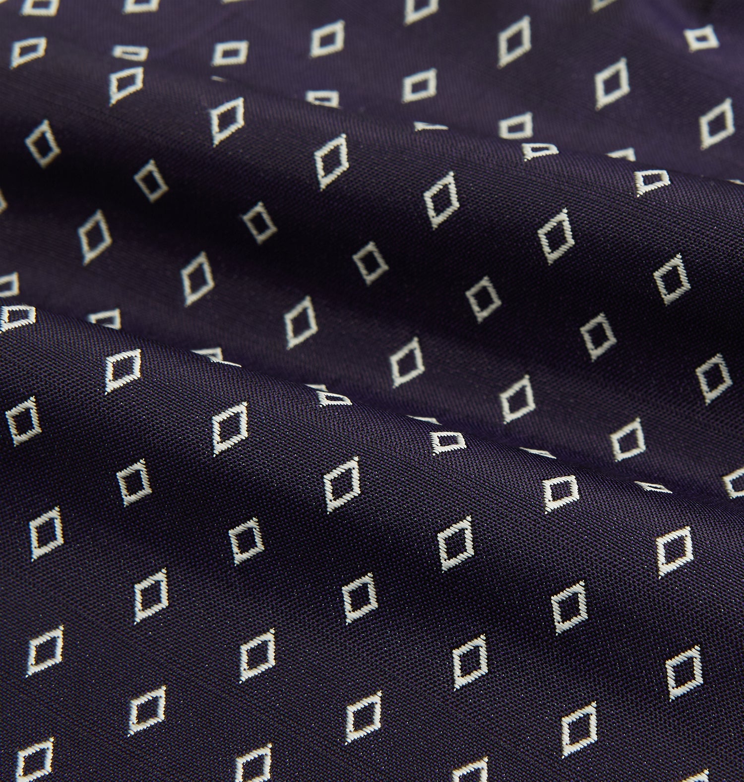 View 4 of product The Turnbull & Asser Blue Diamond Silk Cravat is a refined men's formal accessory, featuring a navy blue base with small white diamond patterns—perfectly complemented by a neatly folded, pointed-corner pocket square.