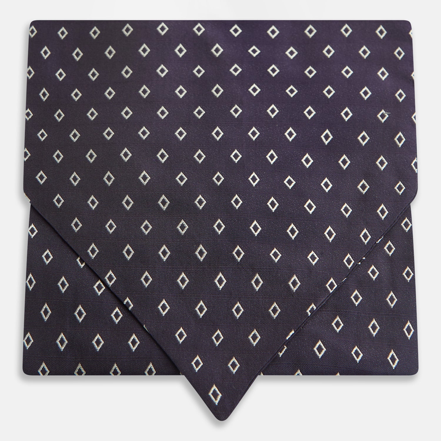 View 1 of product The Turnbull & Asser Blue Diamond Silk Cravat is a refined men's formal accessory, featuring a navy blue base with small white diamond patterns—perfectly complemented by a neatly folded, pointed-corner pocket square.