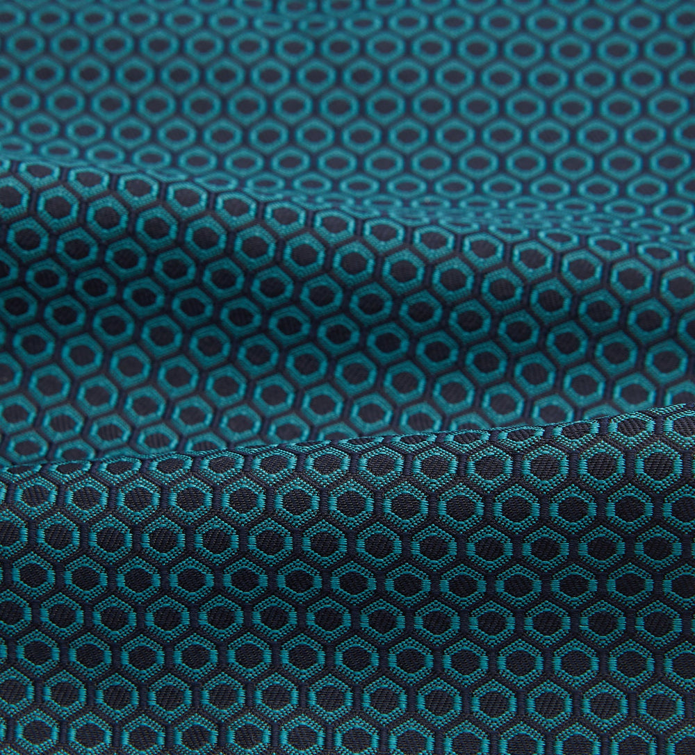 The Turnbull & Asser Turquoise Micro Hexagon Cravat is neatly folded to show a triangular point, displayed with a matching pocket square featuring a subtle hexagon pattern, all set against a white background.