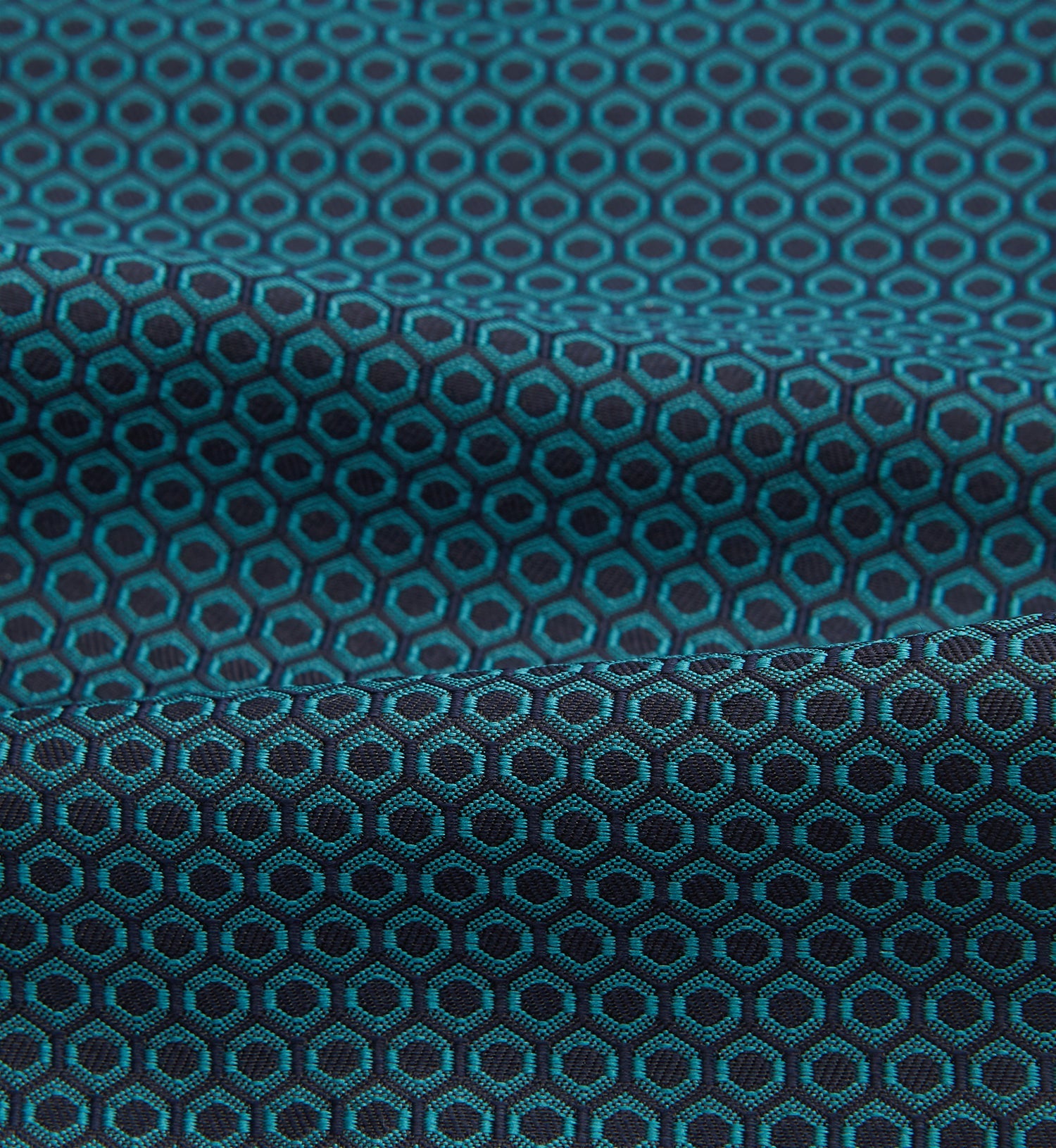 View 4 of product The Turnbull & Asser Turquoise Micro Hexagon Cravat is neatly folded to show a triangular point, displayed with a matching pocket square featuring a subtle hexagon pattern, all set against a white background.