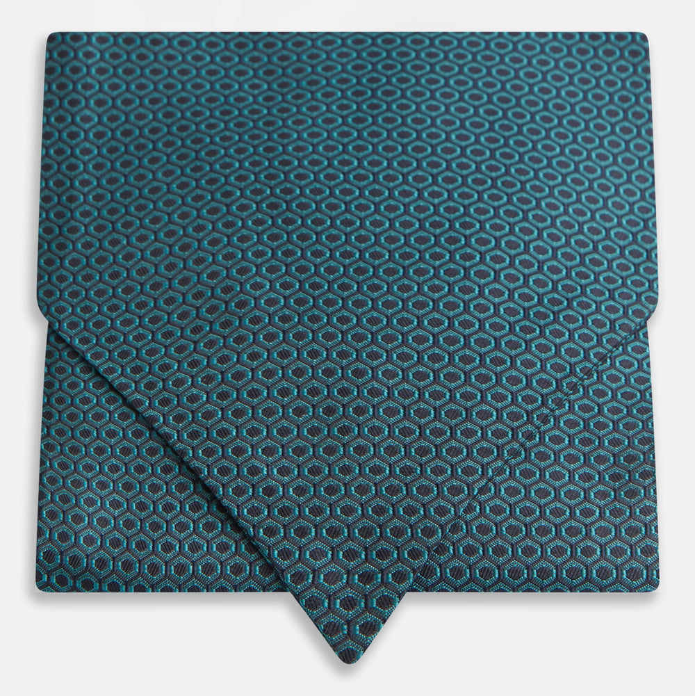 The Turnbull & Asser Turquoise Micro Hexagon Cravat is neatly folded to show a triangular point, displayed with a matching pocket square featuring a subtle hexagon pattern, all set against a white background.