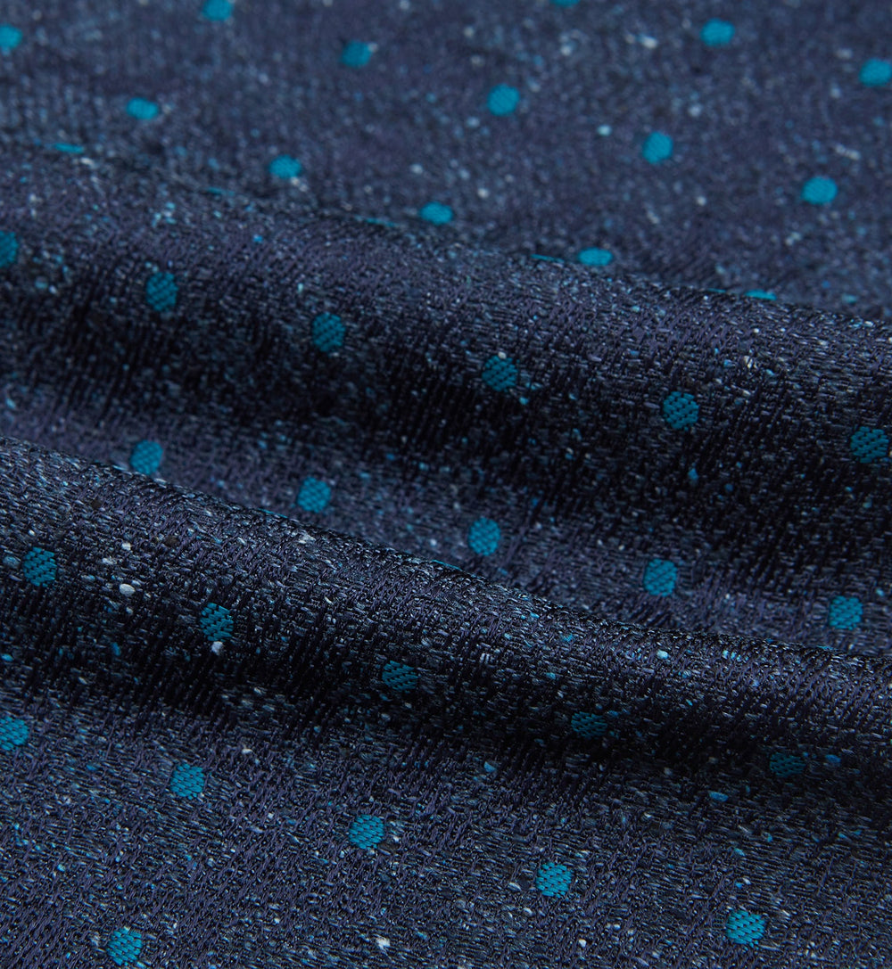 The Teal Micro Dot Silk Cravat by Turnbull & Asser is a formal accessory in textured dark blue silk, with small turquoise polka dots and a pointed edge at the bottom.