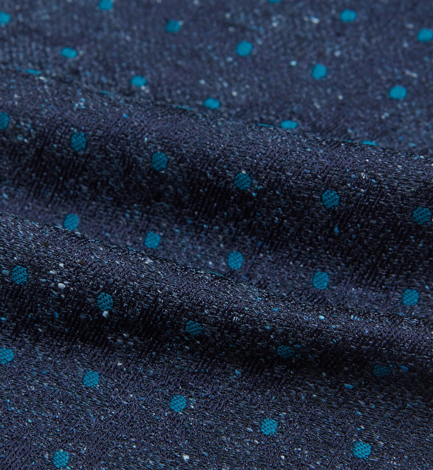 View 4 of product The Teal Micro Dot Silk Cravat by Turnbull & Asser is a formal accessory in textured dark blue silk, with small turquoise polka dots and a pointed edge at the bottom.