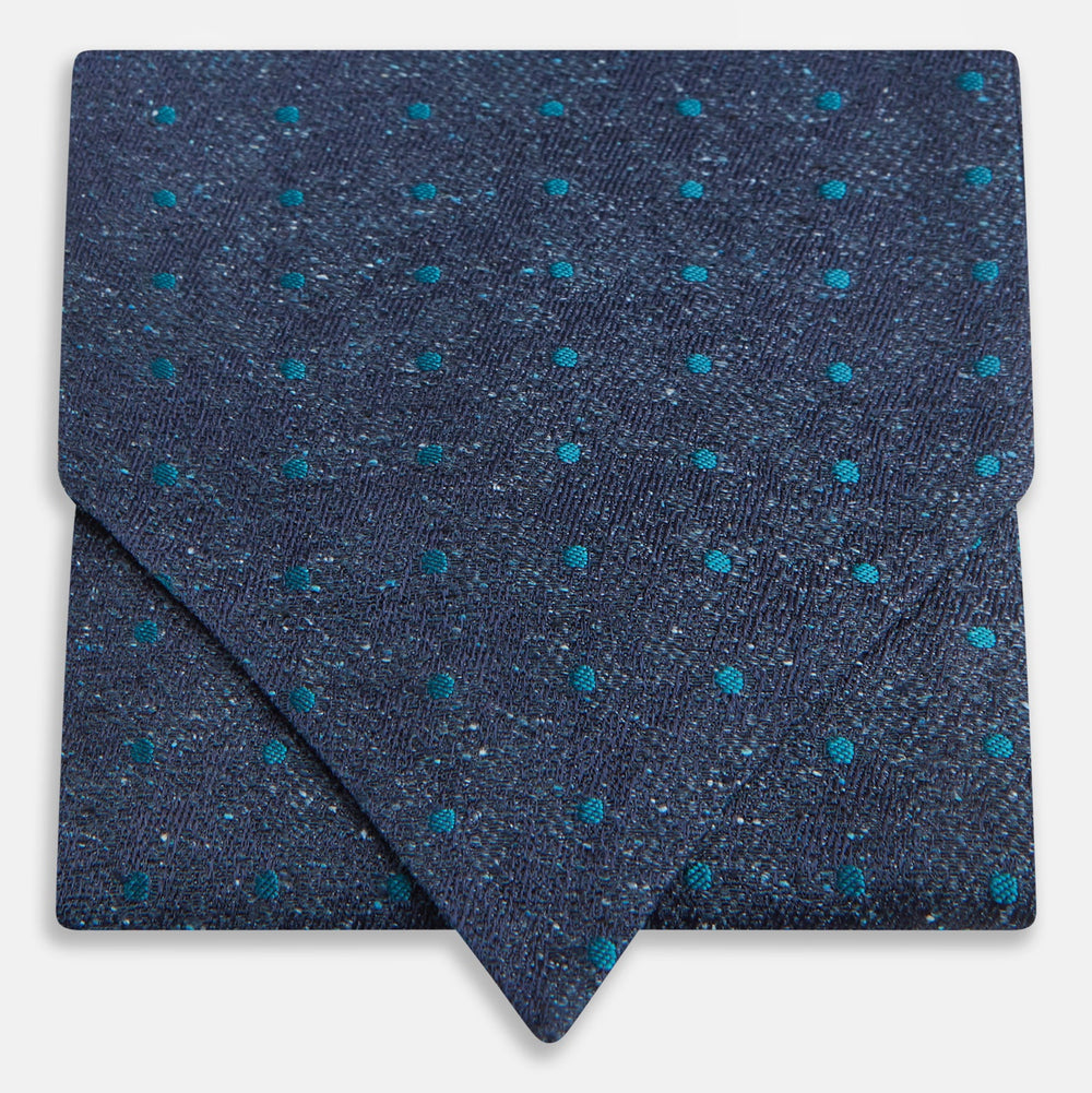 The Teal Micro Dot Silk Cravat by Turnbull & Asser is a formal accessory in textured dark blue silk, with small turquoise polka dots and a pointed edge at the bottom.