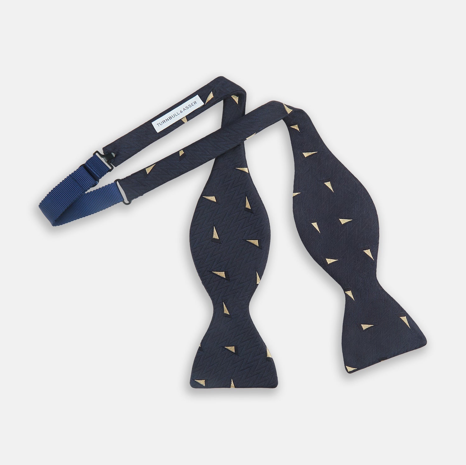 View 2 of product The Navy Triangle Silk Bow Tie by Turnbull & Asser features British elegance with a subtle herringbone pattern and scattered small gold triangle designs.