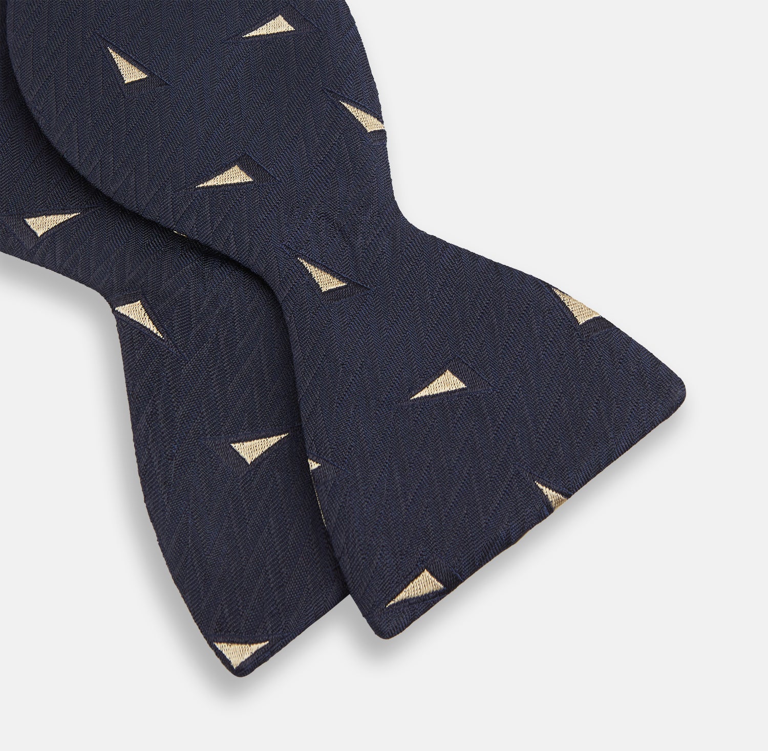 View 3 of product The Navy Triangle Silk Bow Tie by Turnbull & Asser features British elegance with a subtle herringbone pattern and scattered small gold triangle designs.