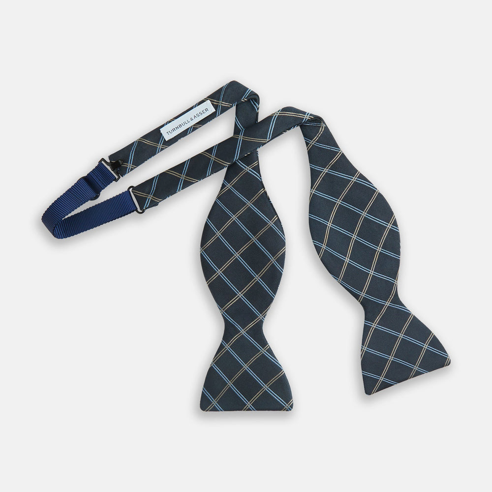 The Turnbull & Asser Navy Triple Check Silk Bow Tie features a navy, light blue, and beige plaid pattern on white, offering British elegance for those who value formal style.