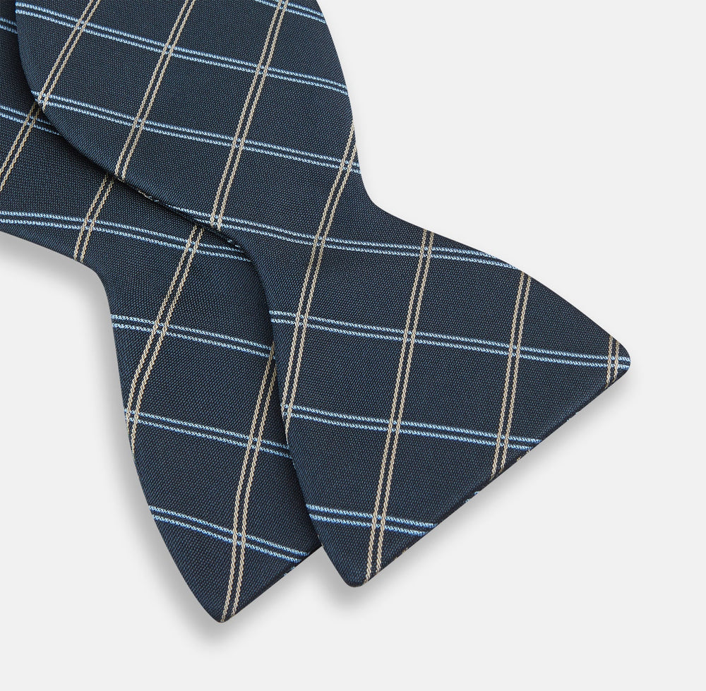 The Turnbull & Asser Navy Triple Check Silk Bow Tie features a navy, light blue, and beige plaid pattern on white, offering British elegance for those who value formal style.