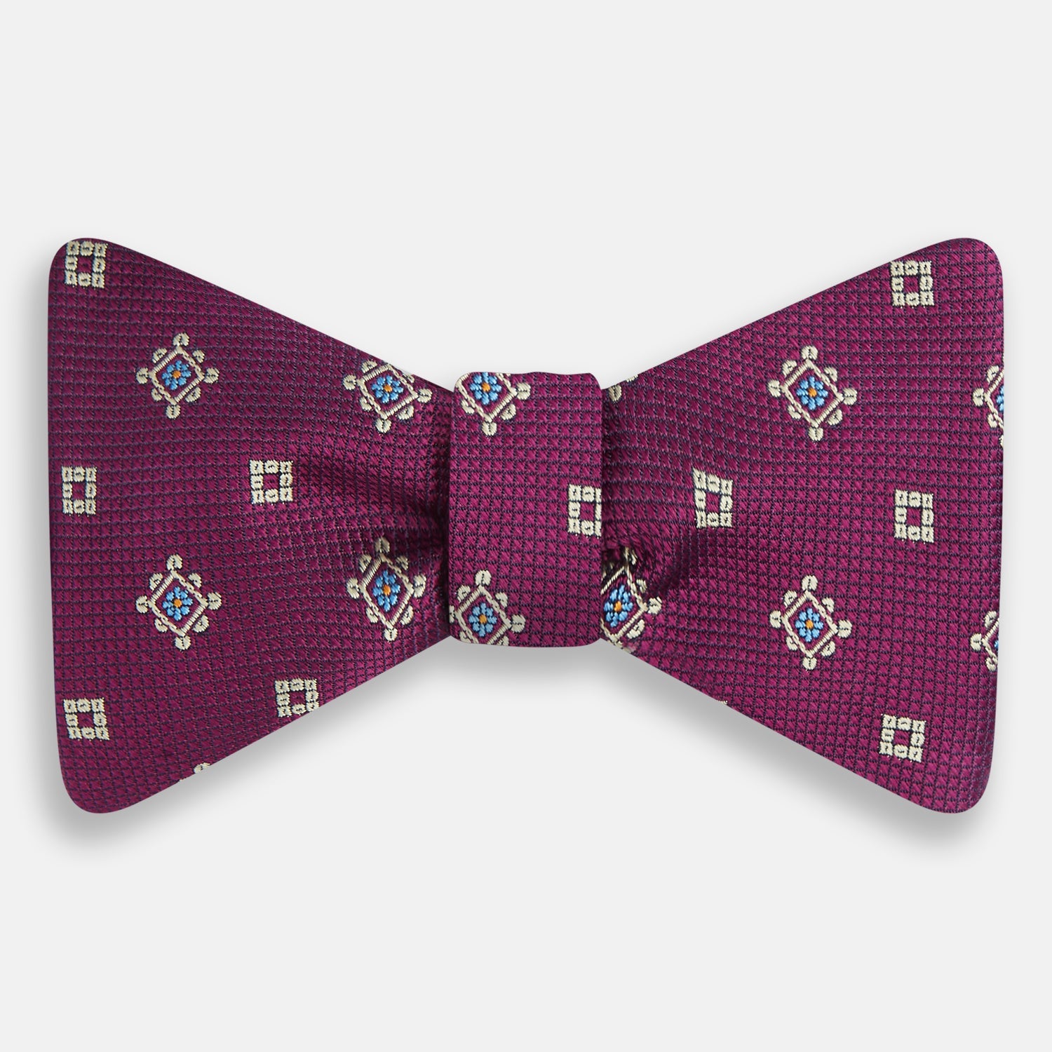 View 1 of product The Magenta Motif Silk Bow Tie by Turnbull & Asser features a textured magenta background with small, square blue, white, and gold geometric designs—an elegant choice for formal occasions.