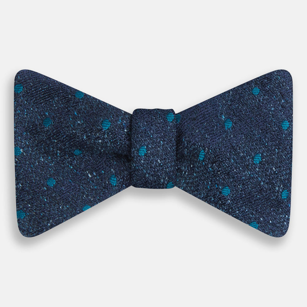 The Turnbull & Asser Teal Micro Dot Silk Bow Tie features textured navy blue silk with small teal dots, showcasing British elegance against a white background.