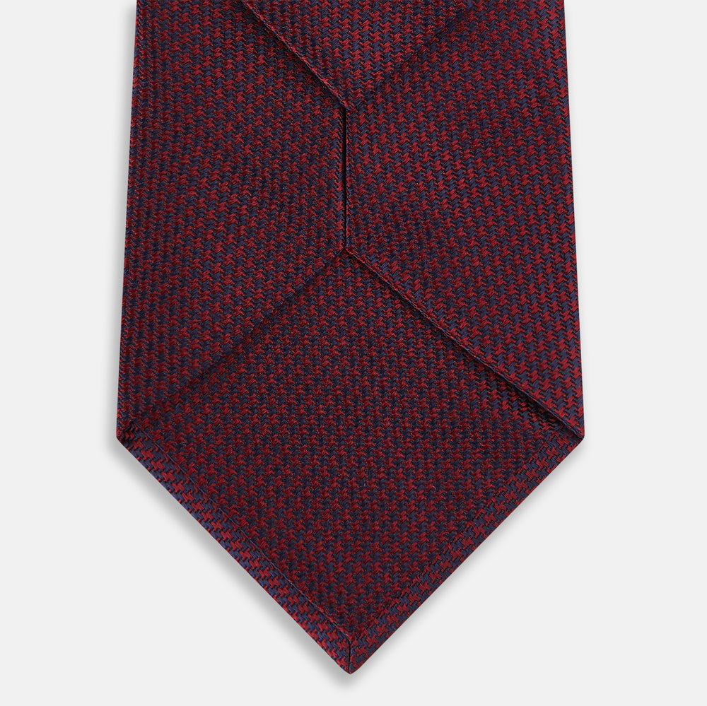 A close-up of the Turnbull & Asser UK Seven-Fold Navy and Red Silk Tie, featuring a small textured check pattern reminiscent of houndstooth, displayed on a plain white background.