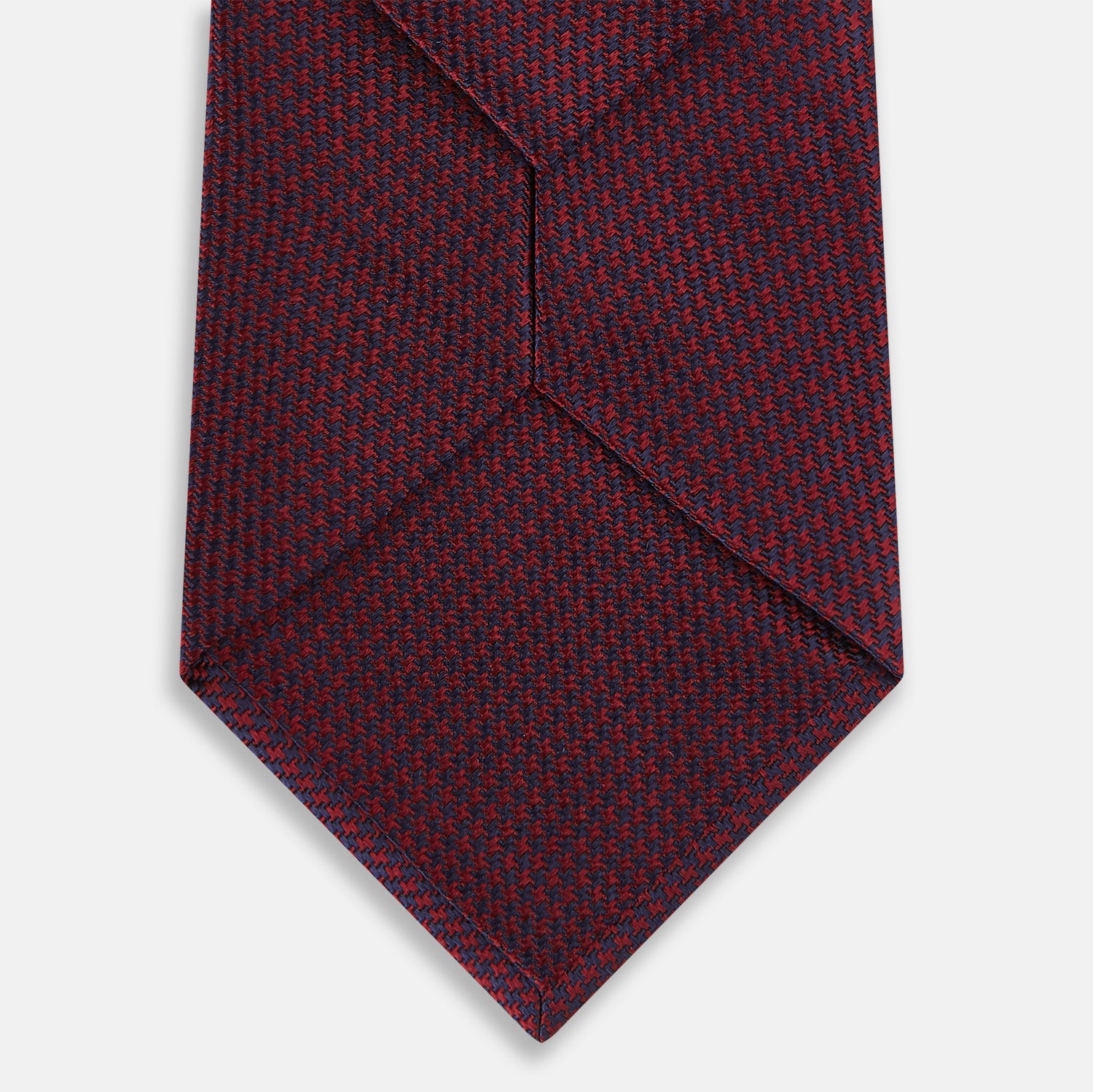 View 3 of product A close-up of the Turnbull & Asser UK Seven-Fold Navy and Red Silk Tie, featuring a small textured check pattern reminiscent of houndstooth, displayed on a plain white background.