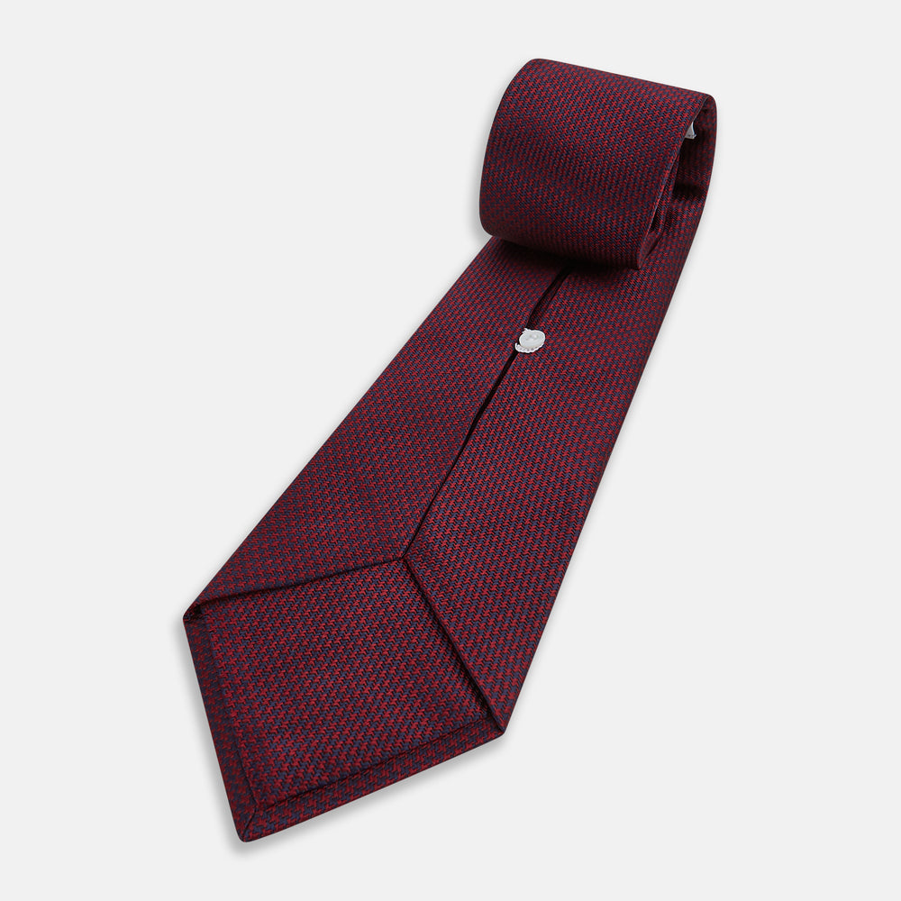 A close-up of the Turnbull & Asser UK Seven-Fold Navy and Red Silk Tie, featuring a small textured check pattern reminiscent of houndstooth, displayed on a plain white background.