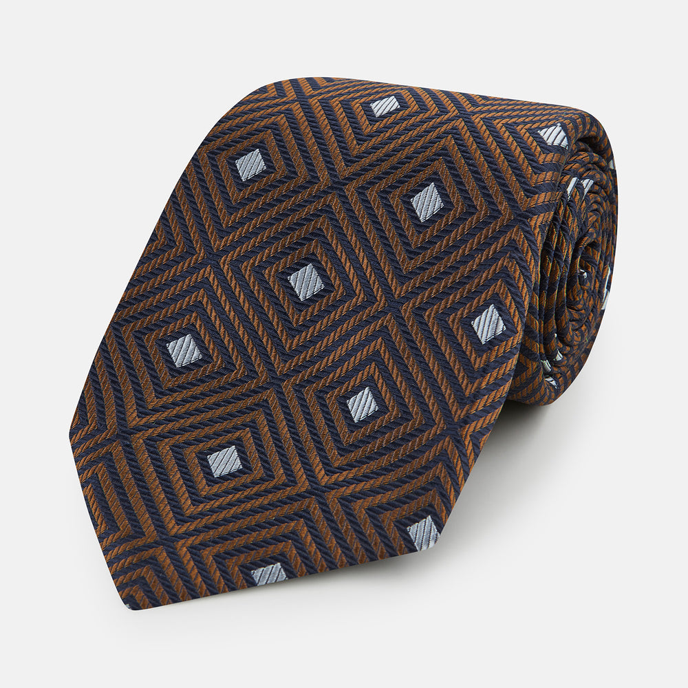The Turnbull & Asser UK Tomorrow Never Dies Seven-Fold Silk Tie, as seen on James Bond, features a navy blue and brown geometric diamond pattern with silver squares at the center, set on a light background.
