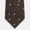 View 4 of product The Turnbull & Asser UK Tomorrow Never Dies Seven-Fold Silk Tie, as seen on James Bond, features a navy blue and brown geometric diamond pattern with silver squares at the center, set on a light background.
