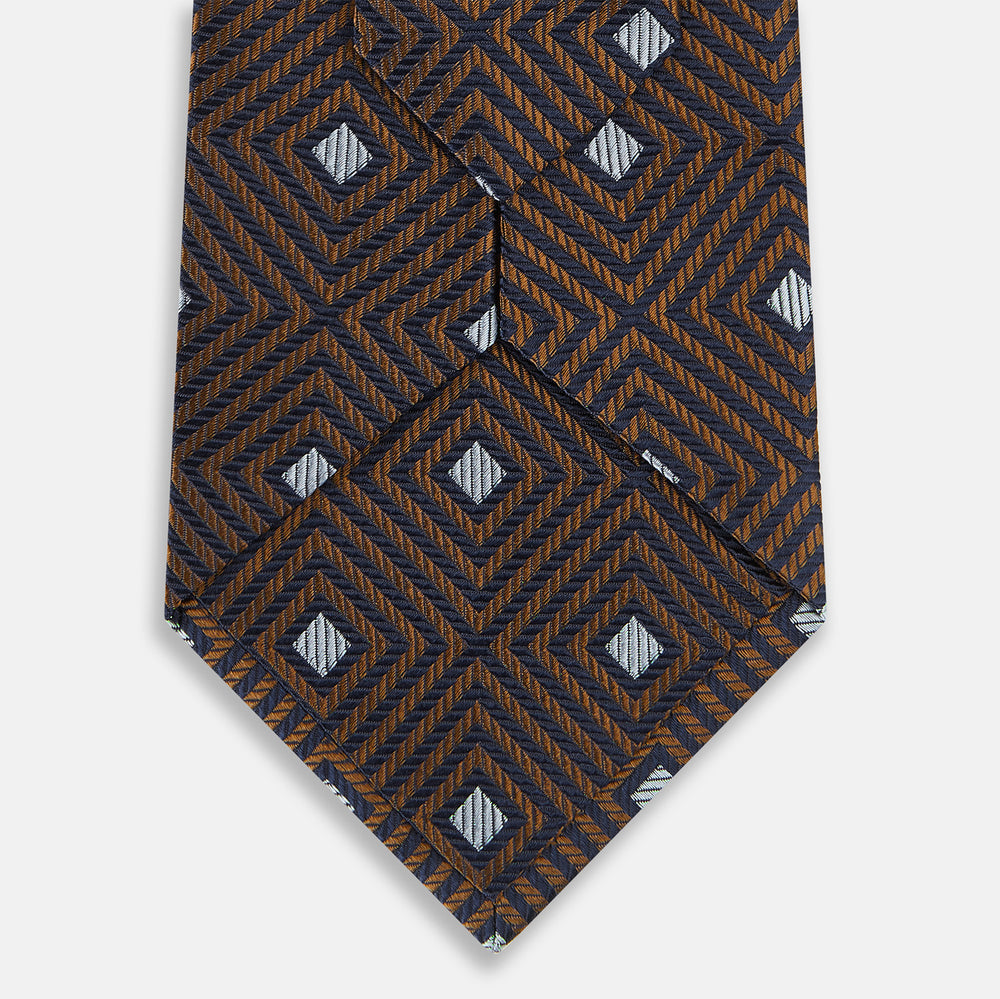 The Turnbull & Asser UK Tomorrow Never Dies Seven-Fold Silk Tie, as seen on James Bond, features a navy blue and brown geometric diamond pattern with silver squares at the center, set on a light background.