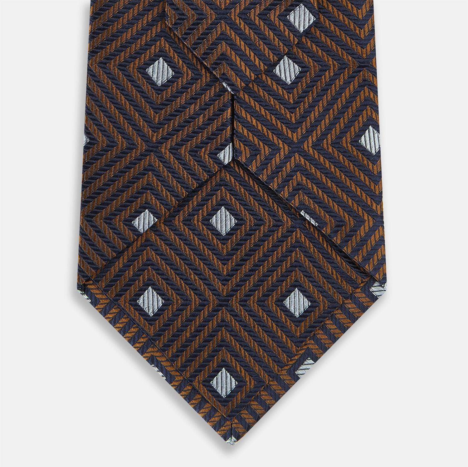 View 4 of product The Turnbull & Asser UK Tomorrow Never Dies Seven-Fold Silk Tie, as seen on James Bond, features a navy blue and brown geometric diamond pattern with silver squares at the center, set on a light background.
