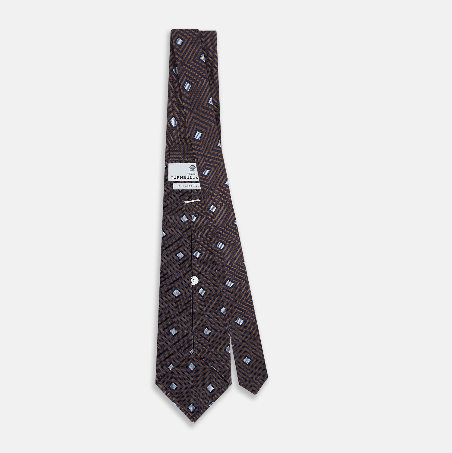 View 4 of product The Tomorrow Never Dies Seven-Fold Silk Tie by Turnbull & Asser UK features a geometric pattern of navy and brown squares with light blue diamond accents, rolled up and displayed on a plain white background.