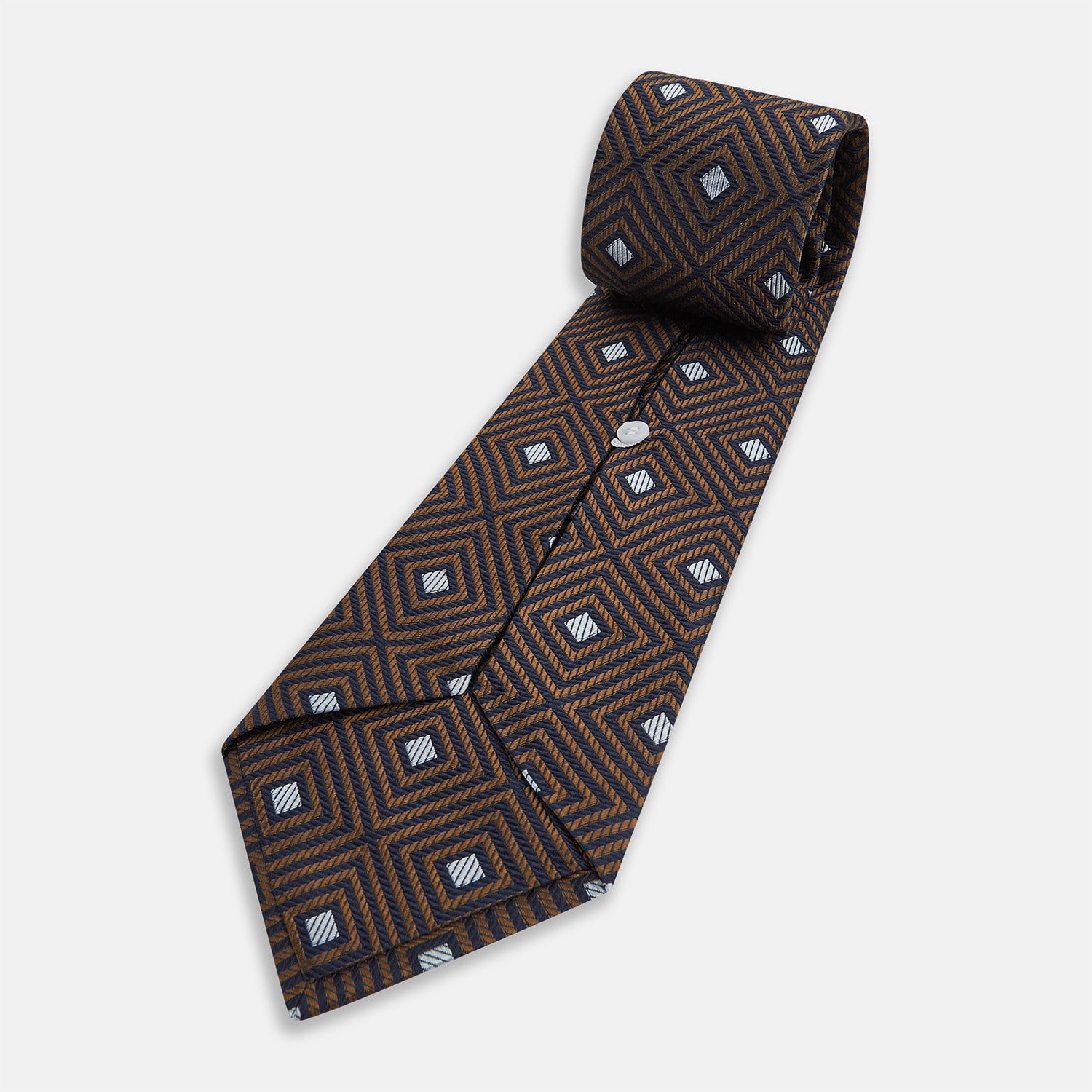 View 5 of product The Turnbull & Asser UK Tomorrow Never Dies Seven-Fold Silk Tie, as seen on James Bond, features a navy blue and brown geometric diamond pattern with silver squares at the center, set on a light background.