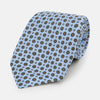 View 1 of product The Turnbull & Asser UK Great Gatsby Seven-Fold Silk Sky Tie, as seen on Jay Gatsby, is a light blue silk tie with a repeating floral medallion pattern in black, yellow, and red circles, shown rolled on a white background.