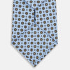 View 3 of product The Turnbull & Asser UK Great Gatsby Seven-Fold Silk Sky Tie, as seen on Jay Gatsby, is a light blue silk tie with a repeating floral medallion pattern in black, yellow, and red circles, shown rolled on a white background.